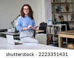 Young happy smiling professional business woman, female company worker or corporate manager holding digital tablet technology posing in modern office working, looking at camera, portrait.