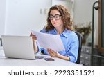 Small photo of Young busy business woman manager, lawyer or company employee holding accounting bookkeeping documents checking financial data or marketing report working in office with laptop. Paperwork management