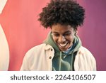Small photo of Authentic candid shot of young happy African American cool teen guy laughing on red wall lit with sunlight. Smiling cool rebel gen z teenager model standing outdoors having fun, portrait outdoors.