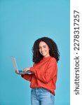 Small photo of Young happy latin woman using laptop device isolated on blue background. Smiling female model user holding computer presenting advertising job search or shopping website, online services, vertical.