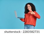 Small photo of Young happy latin woman pointing at laptop isolated on blue background. Smiling female model holding computer presenting advertising job search or ecommerce shopping website.