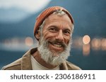 Happy older bearded man standing in nature park outdoors and laughing. Smiling active mature senior traveler looking at camera advertising camping tourism. Close up face front portrait.