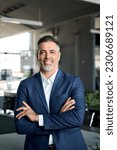 Small photo of Happy mid aged business man ceo standing in office arms crossed. Smiling mature confident professional executive manager, proud confident businessman leader wearing blue suit, vertical portrait.