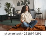 Young calm latin woman doing yoga exercise at home feeling zen. Mindful girl sitting on floor meditating chilling with eyes closed, relaxing breathing for good mental balance, peace of mind.