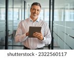 Small photo of Happy mature european business man manager standing in office hall using digital tablet. Mid aged businessman professional executive holding tab looking at camera, working on financial data, portrait.