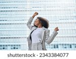 Small photo of Happy excited confident professional young African American business woman office leader executive wearing suit celebrating financial goals standing in big city street feeling success and freedom.