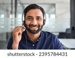 Small photo of Happy Indian man call center agent wearing headset in office. Smiling male contract service representative telemarketing operator looking to camera working in customer support. Headshot portrait.