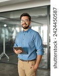 Small photo of Smiling busy young latin business man company manager using tablet computer, happy hispanic businessman executive looking at camera holding tab working standing in office. Vertical portrait.