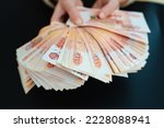 Small photo of a woman holds in her hands a fan of banknotes of 5000 rubles on a black background. the concept of depreciation of the ruble. earnings online in Russia.
