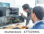 Businessmen trading stocks online. Stock brokers looking at graphs, indexes and numbers on multiple computer screens. Colleagues in discussion in traders office. Business success concept.