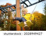 Little boy having fun on a swing on the playground in public park on autumn day. Happy child enjoy swinging. Active outdoors leisure for child in city