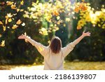 Young woman is having fun while walking through the forest on a sunny autumn day. Girl plays with maple leaves and throws them up. Fallen leaves rustle.