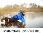 A cute preschooler fell on the ice of a frozen lake or river at a cold sunny winter sunset. Danger of children's outdoor games in winter