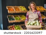 Small photo of Woman works in fruits and vegetables shop. She is holding basket with marrow squash.
