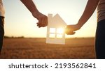 Small photo of paper house happy family. friendly family hands holding paper house the glare of the sun shine through the window a beautiful sunset. mortgage business construction concept lifestyle. house dreams