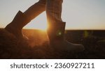 Small photo of farmer feet walks across a lifestyle black field. agriculture business concept. silhouette of a farmer feet at sunset walking across black plowed field. farmer in rubber boots legs close-up