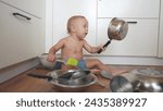 Small photo of baby playing pots in the kitchen on floor. happy family kid dream concept. baby scattered pots play dabble sitting on the floor. baby scattered dishes pots sunlight mess