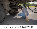 Small photo of 18-Wheeler Pre-trip Tire Inspection - A professional driver is using a tire thumper to check the tires underneath his trailer prior to driving OTR.