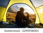 View from inside a tent of hiker drink hot tea and looking to the mountains valley with ice glacier landscape at sunset during trekking in Central Asia Kazakhstan, Almaty