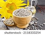 Small photo of Sunflower flour in bowl, oil in decanter, seeds in a spoon on burlap, sunflower flower on wooden board background
