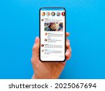 Small photo of Person holding phone in hand with sample social media news feed on the screen