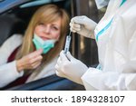 Woman sitting in car, waiting for medical worker to perform drive-thru COVID-19 test, taking nasal swab sample through car window, PCR diagnostic for Coronavirus, doctor in PPE holding test kit.