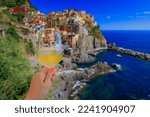 Woman holding a glass of white wine with Mediterranean Sea and traditional colorful houses in romantic old town of Manarola in Cinque Terre, Italy