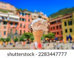 Hand holding an artisanal gelato, a view of traditional colorful houses in old town of Vernazza in Cinque Terre on the Mediterranean Sea, Italy