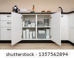 Dishware storage cabinet with open doors, white plates, bowls cups and other china crockery inside, front view
