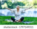 Mindful senior woman, feeling overwhelmed by beauty of the, meditating, sitting by the water with open arms