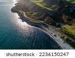 Small photo of Causeway Coastal Route a.k.a Antrim Coast Road A2 on the Atlantic coast in Northern Ireland. One of the most scenic coastal roads in Europe. Aerial view against the rising sun in winter