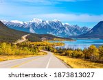 Small photo of Asphalt highway leads to Abraham Lake in the Canadian Rockies. The yellow foliage of birches and aspens is mixed with green conifers. The first snow has already fallen on the peaks