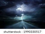 Extreme weather conditions. An empty landscape with a road leading into a powerful thunderstorm with lightning strikes. Photo composition.