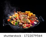 Assorted delicious grilled meat with vegetables on barbecue grill with smoke and flames isolated on black background