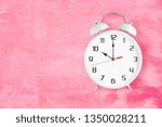 Small photo of Old fashioned alarm clock with twin bells and ringer showing 10 ten o'clock on pink texture as background