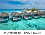 Aerial view of Maldives island, luxury water villas resort and wooden pier. Beautiful sky and ocean lagoon beach background. Summer vacation holiday and travel concept. Paradise aerial landscape pano