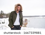 Handsome bearded young caucasian man standing outdoors fur hood in winter season forest. Attractive stylish european guy walking snowy christmas woodland Season holiday leisure                       