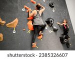 Small photo of Mother and daughter climbing wall in gym. Adult woman and her child climb on climbing center. Trainer with young child climbs training climbing wall. Family on training climbing center