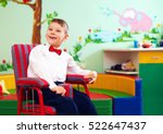 Small photo of cute happy kid in wheelchair, wearing glad rags in center for children with special needs