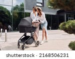 Talking and having fun. Two female friends having a walk with baby carriage outdoors.