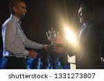 Side view of Caucasian businessman giving trophy to mixed race business male executive on stage in auditorium