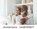 Front view of senior diverse couple sitting on a white couch in beach house. Authentic Senior Retired Life Concept
