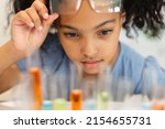 Small photo of Close-up of biracial elementary schoolgirl looking at chemicals in test tubes during chemistry class. unaltered, education, learning, scientific experiment, stem, protection and school concept.