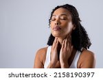 Small photo of African american mid adult woman with eyes closed touching painful throat against white background. copy space, throat, thyroid, medical, pain, sickness and healthcare concept.