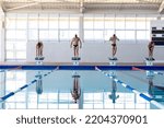 Small photo of Front view of four male swimmers at swimming pool, standing on starting blocks, ready to plunge into water. Swimmers training hard for competition.