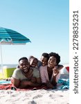 Small photo of African american parents with children laughing and lying on towels at beach under clear sky. Copy space, unaltered, family, together, parasol, picnic, nature, vacation, enjoyment, relaxing, summer.