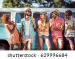 Group of happy friends standing with ice lolly in front of camper van in park