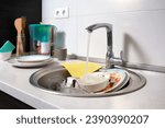 Small photo of Close-up of a kitchen sink with dirty dishes. Water flows from an open tap. Reluctance to do routine housework after dinner.