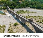 Small photo of Aerial view. Drought and dry rivers. Roman bridge of Bobbio over the Trebbia river, Piacenza, Emilia-Romagna. Italy. 06-16-2022. River bed with stones and vegetation. Called hunchback bridge