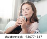 Young woman sitting on couch at home and drinking coffee, casual style indoor shoot